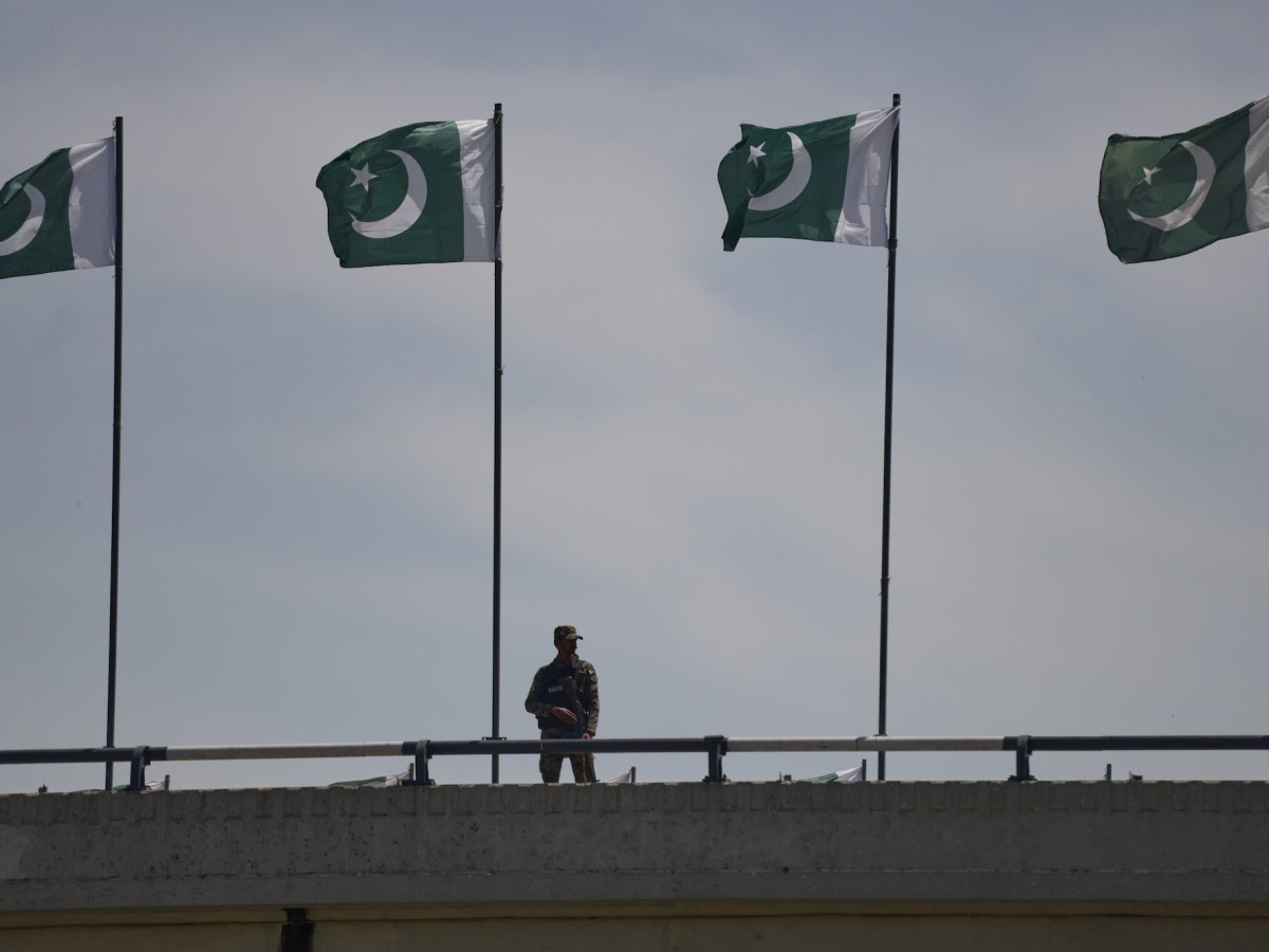 A soldier stands on a bridge with 4 green and white Pakistani flags flying from poles