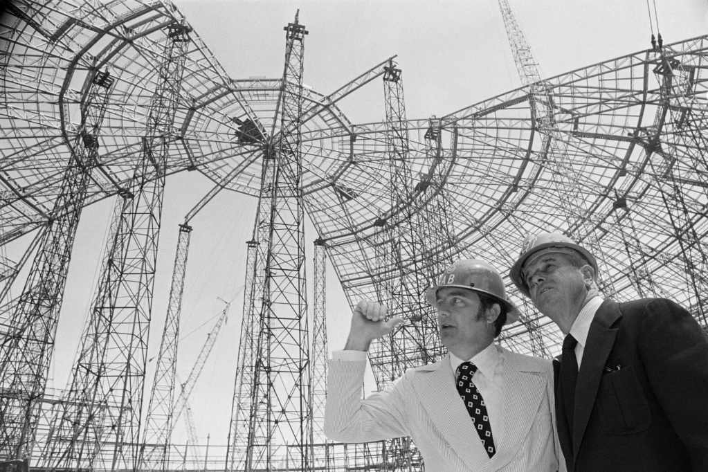An older black and white photo of two men wearing suits and hardhats on a construction site