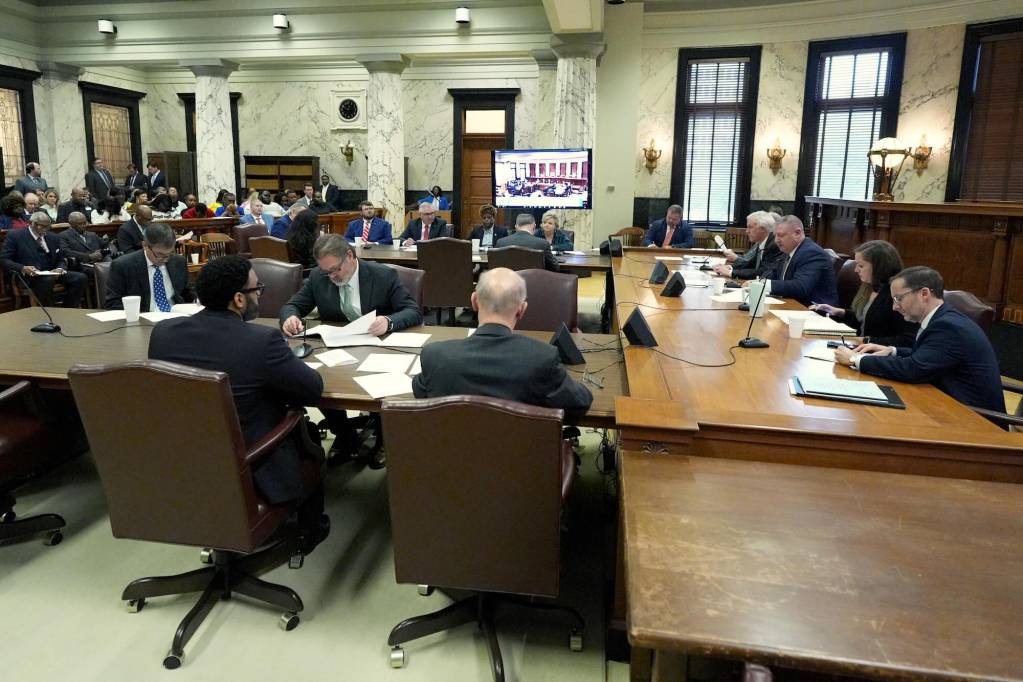 A senate committee meeting with people sitting at all desks, reading papers and discussing issues