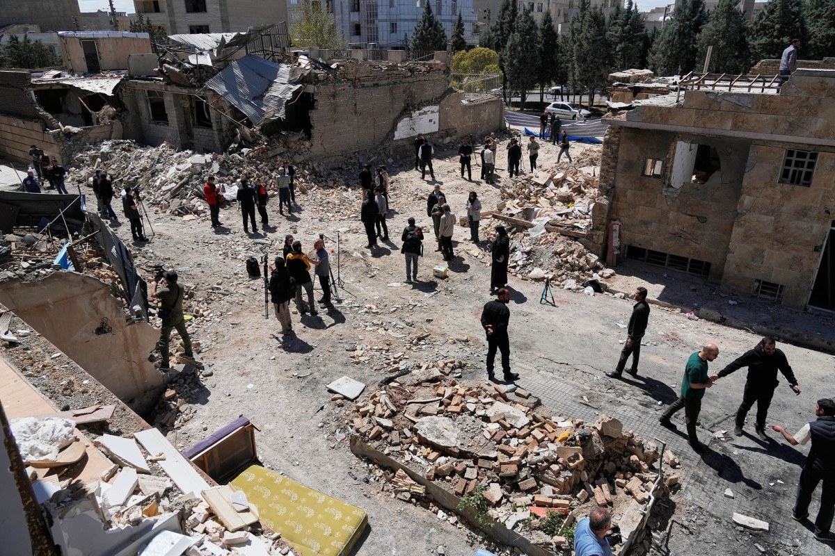 A group of people surveying a block of damaged buildings with rubble covering the ground.
