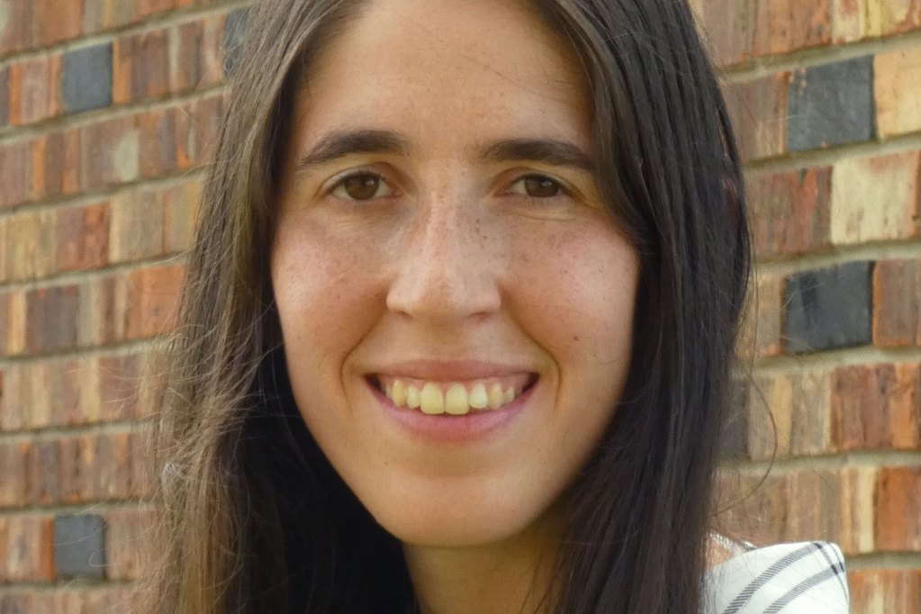 A closeup of a person with long brown hair standing in front of a brick wall