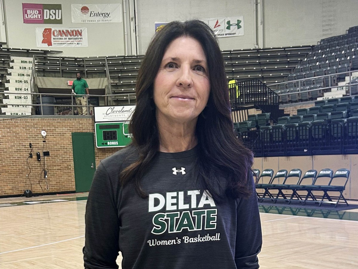 A woman wearing a sweatshirt with “Delta State Women’s Basketball” standing on a basketball court.