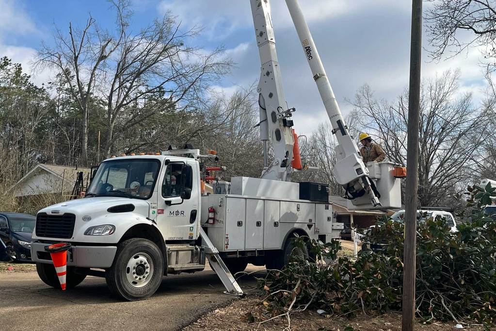 A white utility vehicle works on poles surrounded by a large pile of cut tree limbs