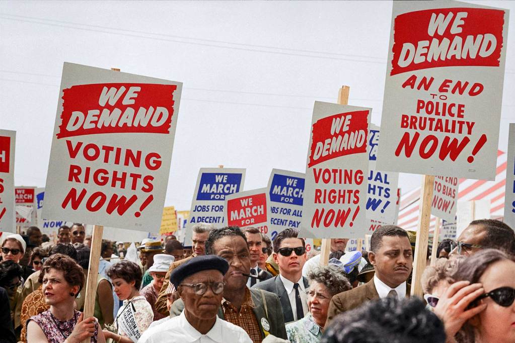 A large group of people marching with signs that say “We Demand Voting Rights Now!” and “We Demand An End To Police Brutality Now!”
