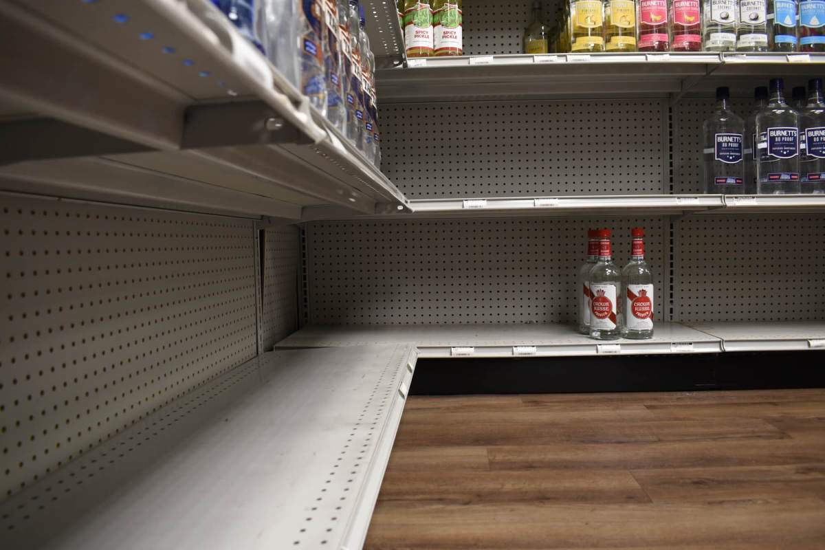 A low view of shelves at a liquor store, the bottom shelf only having three bottles and the shelf above has a big gap in product