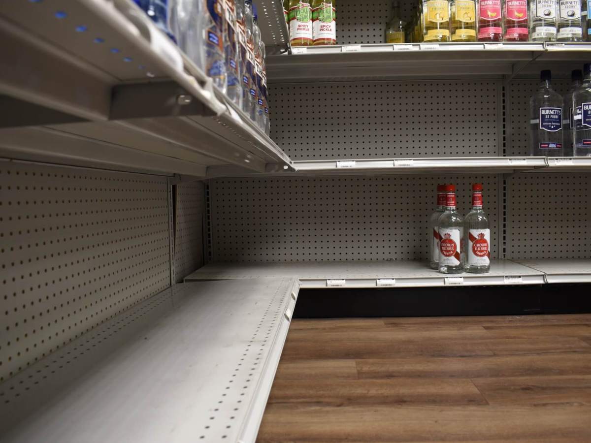 A low view of shelves at a liquor store, the bottom shelf only having three bottles and the shelf above has a big gap in product
