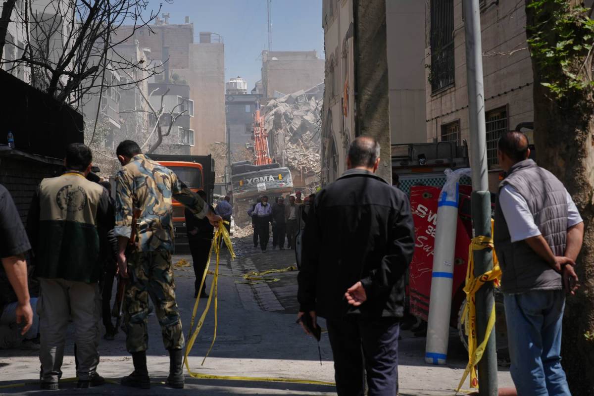 A group of people looking down a street with several damaged buildings.