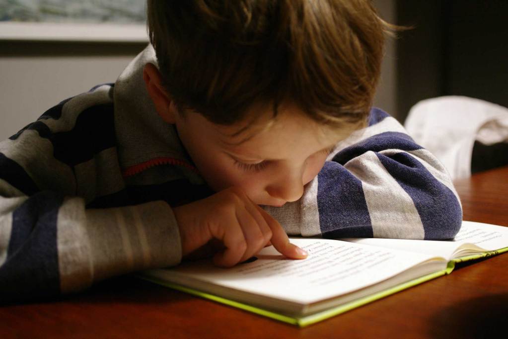 A young boy reading a book, using his finger to guide his eyes to the words on the page.