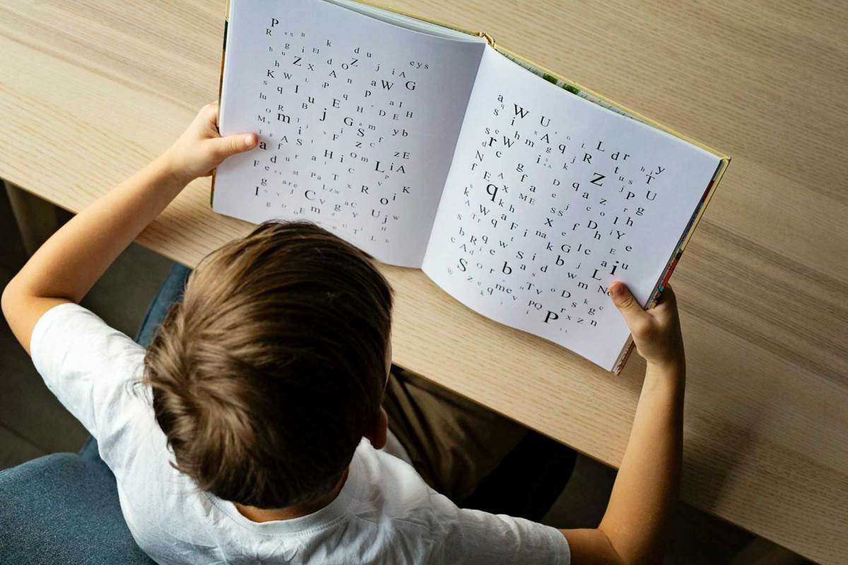 An overhead view of a young girl reading a book. Letters with different fonts and typefaces are on the pages.
