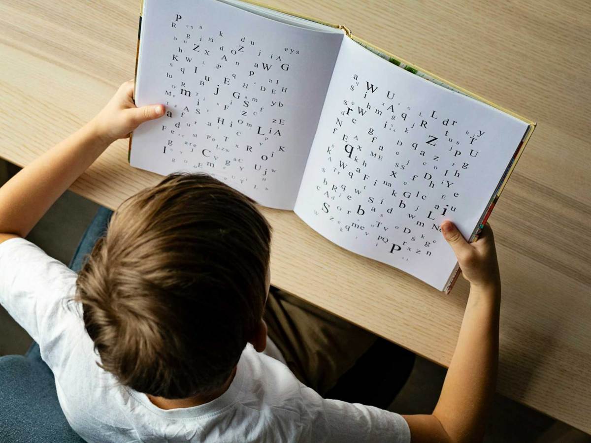 An overhead view of a young girl reading a book. Letters with different fonts and typefaces are on the pages.