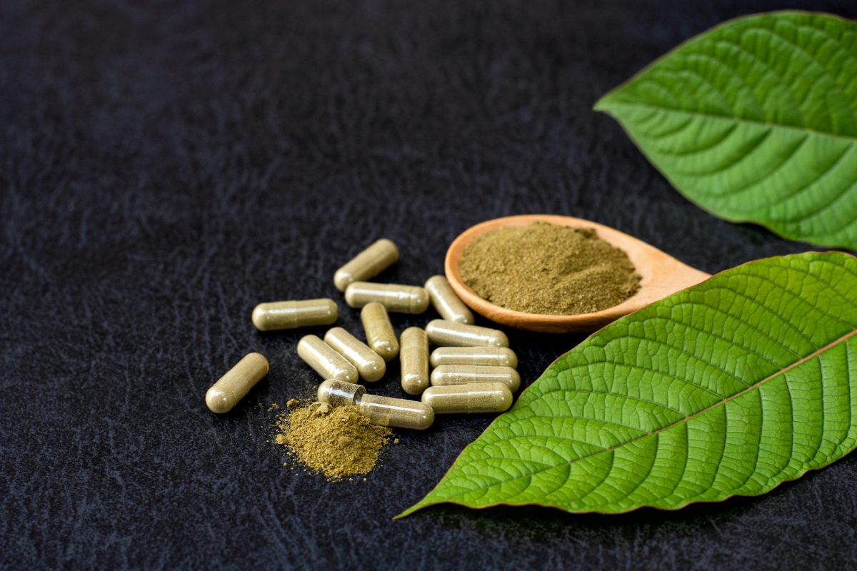 A set of pills next to a fine, brown powder and a green leaf