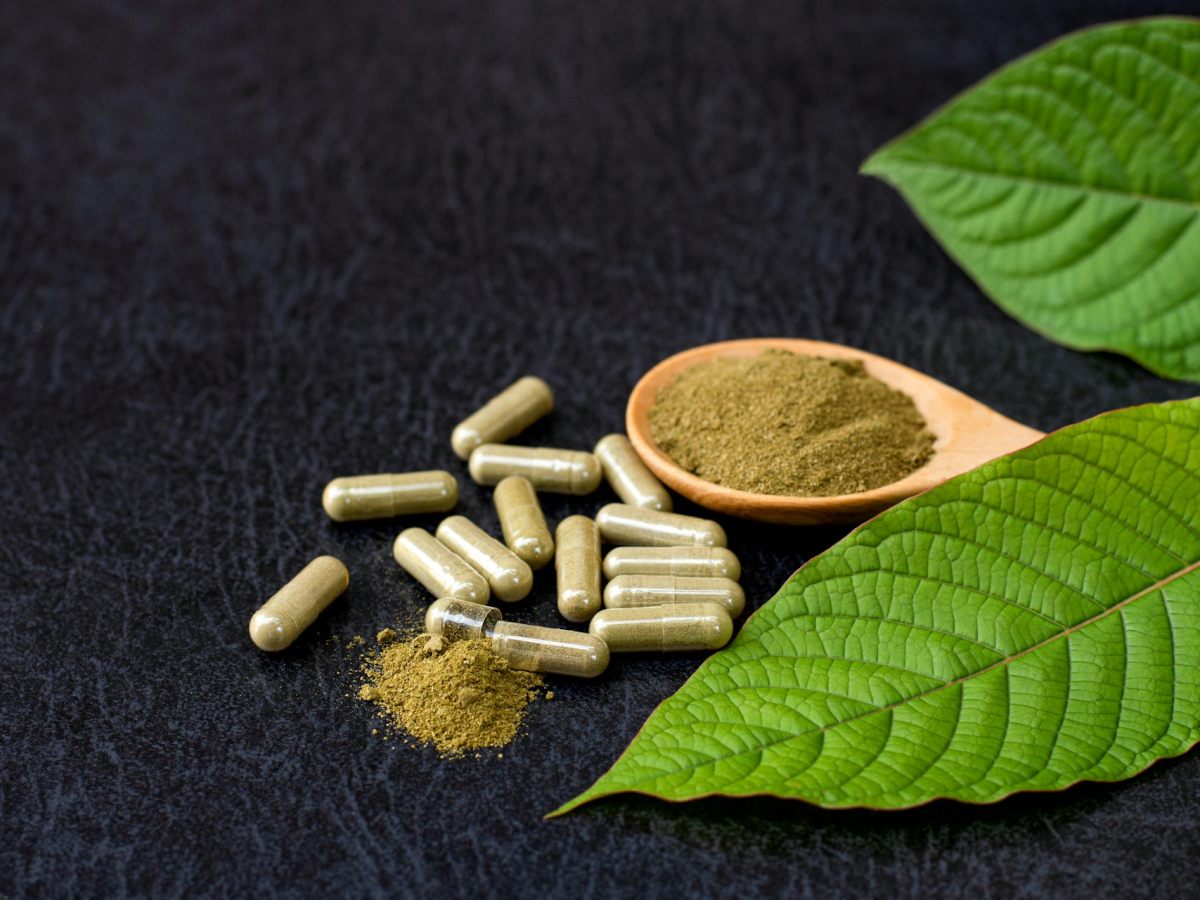 A set of pills next to a fine, brown powder and a green leaf