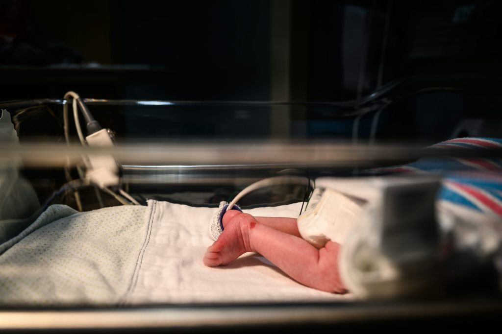 An infant child’s legs seen as it lays in a hospital bassinet.