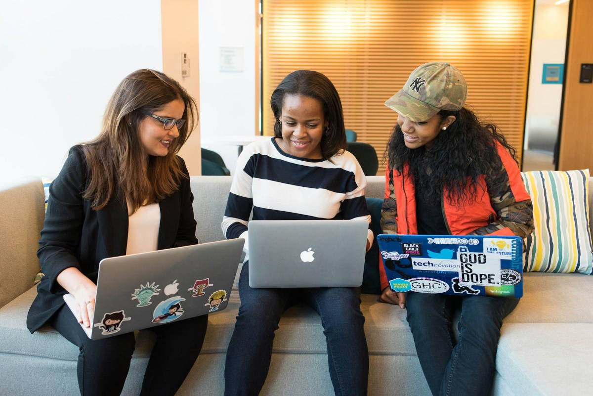 Three women seated together, each working on a laptop