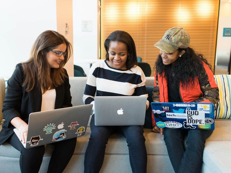 Three women seated together, each working on a laptop