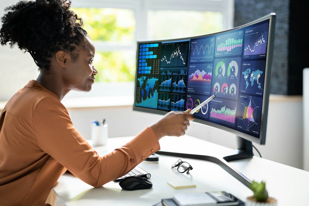 A woman seated in front of several computer monitors with graphical displays.