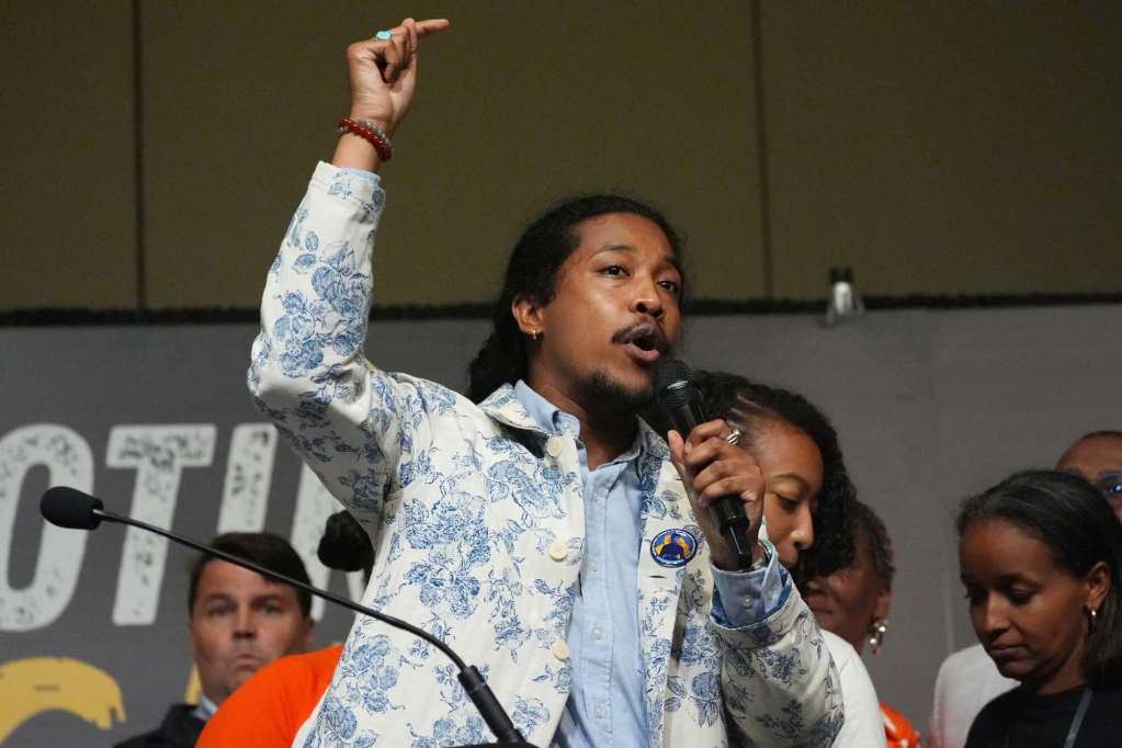 Justin Jones speaks at an event with mic in hand, the other arm pointing up over his head