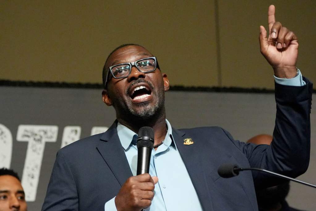A closeup of Bryant Clark speaking on stage, mic in one hand and the other hand pointing up