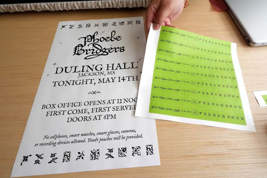 A flyer for Phoebe Bridgers at Duling Hall and a hand holding a page of uncut green wristbands