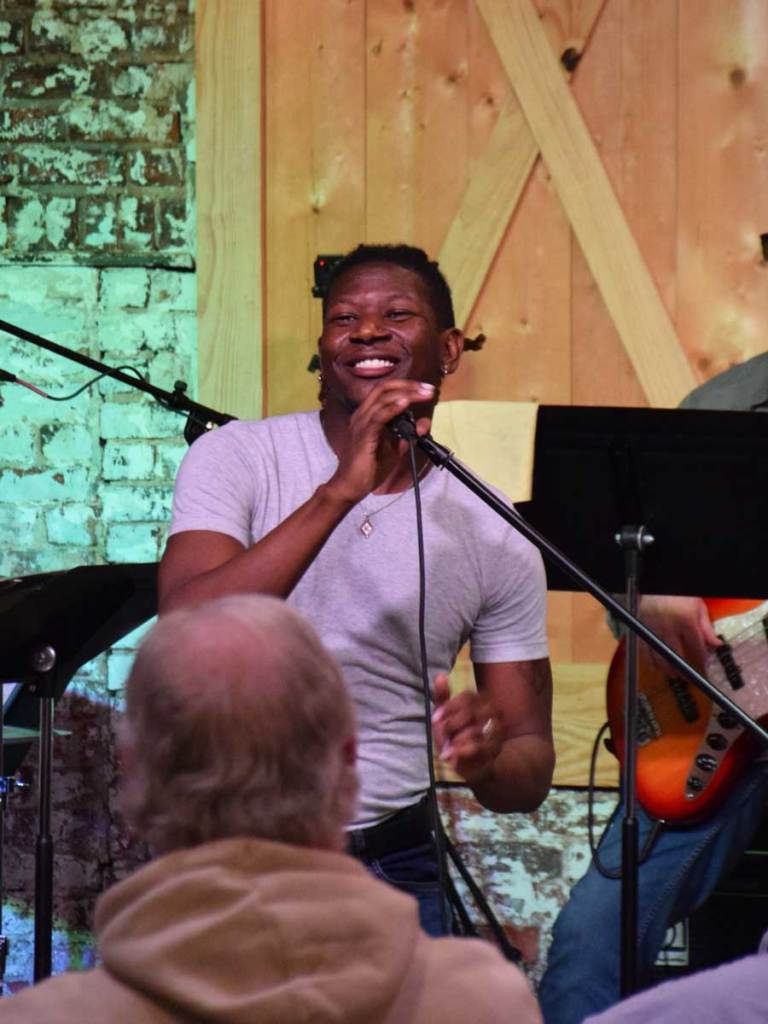 Dre Walker performs a song for the crowd at a nighttime show inside a brick room.