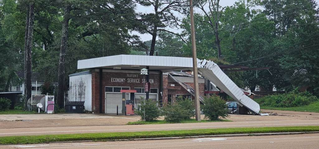 A gas station with a sign that reads 'Economy Service Station' showing signs of tornado damage to the roof
