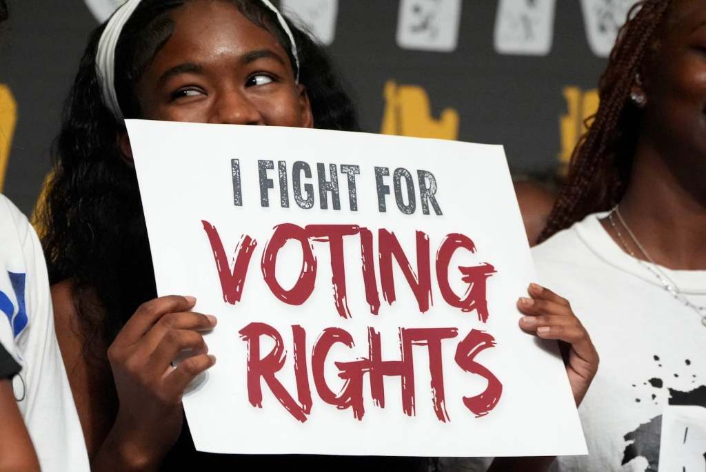 A woman holds up a sign that reads 'I Fight For Voting Rights'