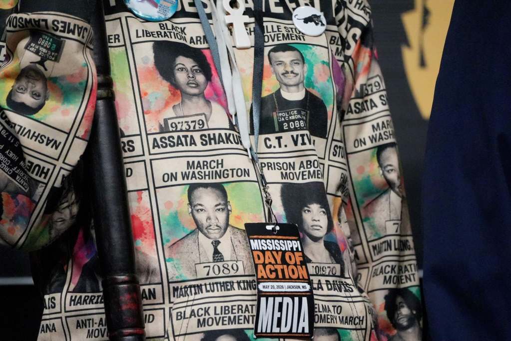 A closeup of a person's shirt showing the booking photos of various civil rights leaders. Also seen is a media pass for Mississippi Day of Action hanging around their neck