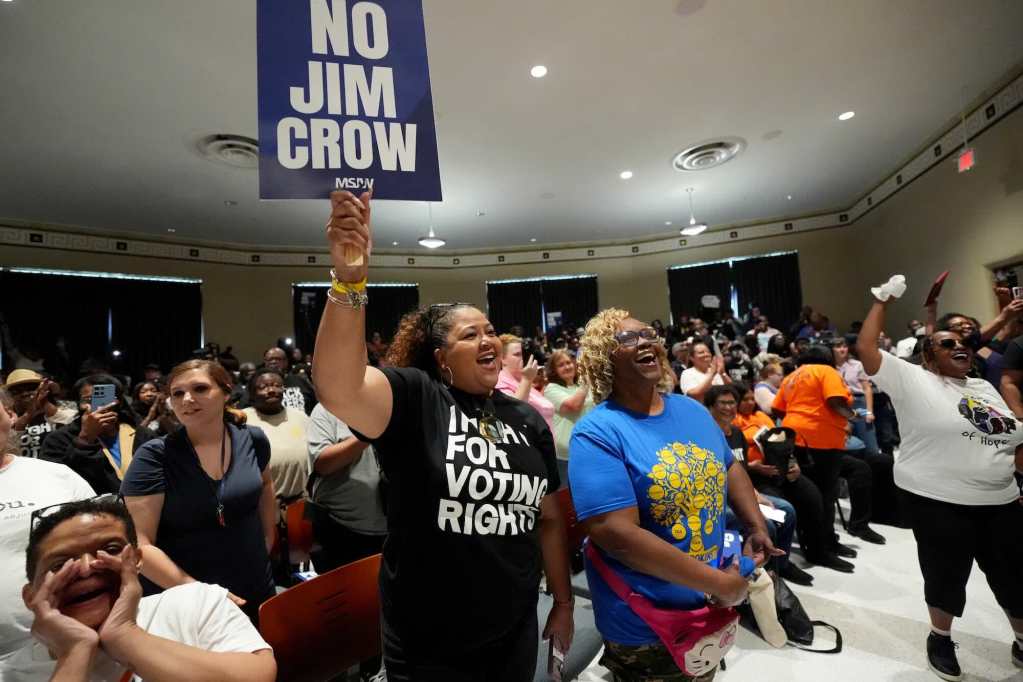 A room filled with standing people, one holding a sign that says 'No Jim Crow'