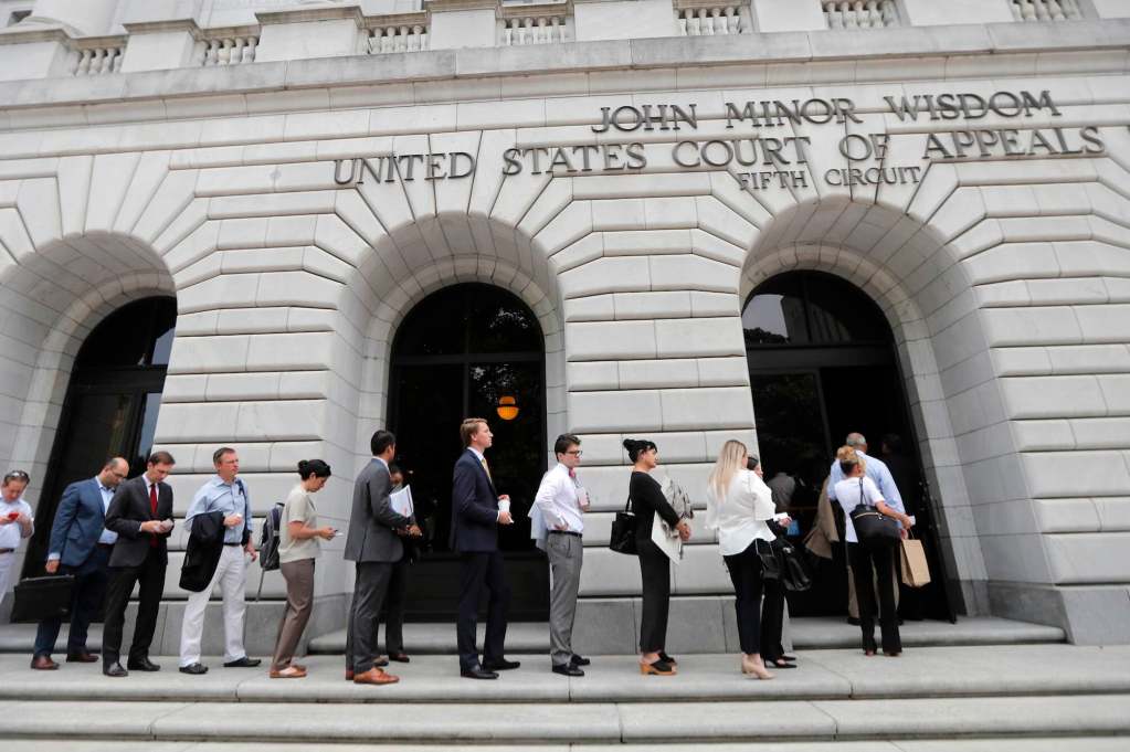 People seen lined up to enter a white building labeled John Minor Wisdom - United States Court of Appeals - Fifth Circuit