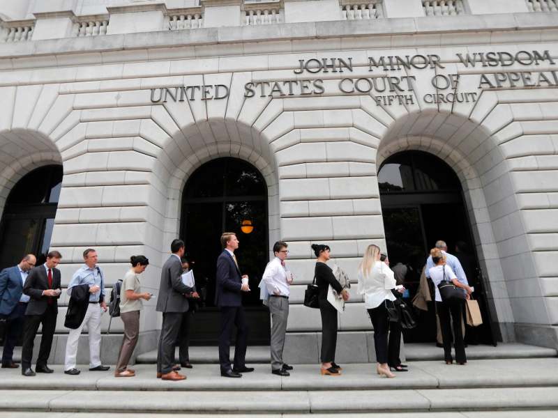 People seen lined up to enter a white building labeled John Minor Wisdom - United States Court of Appeals - Fifth Circuit