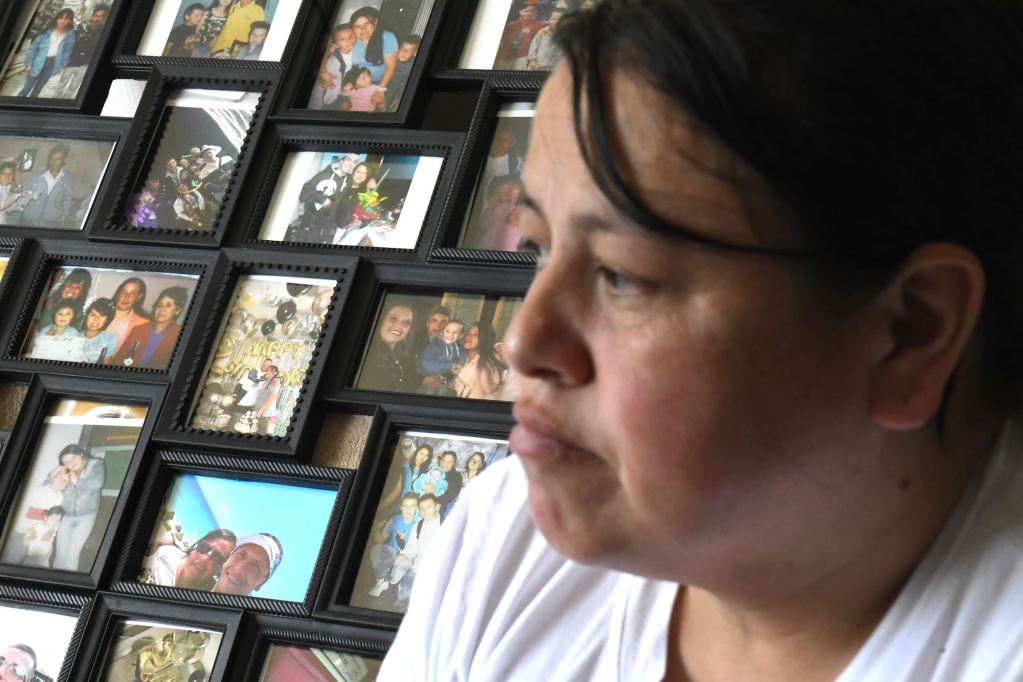 A woman sits in her home with numerous framed photos in the background.