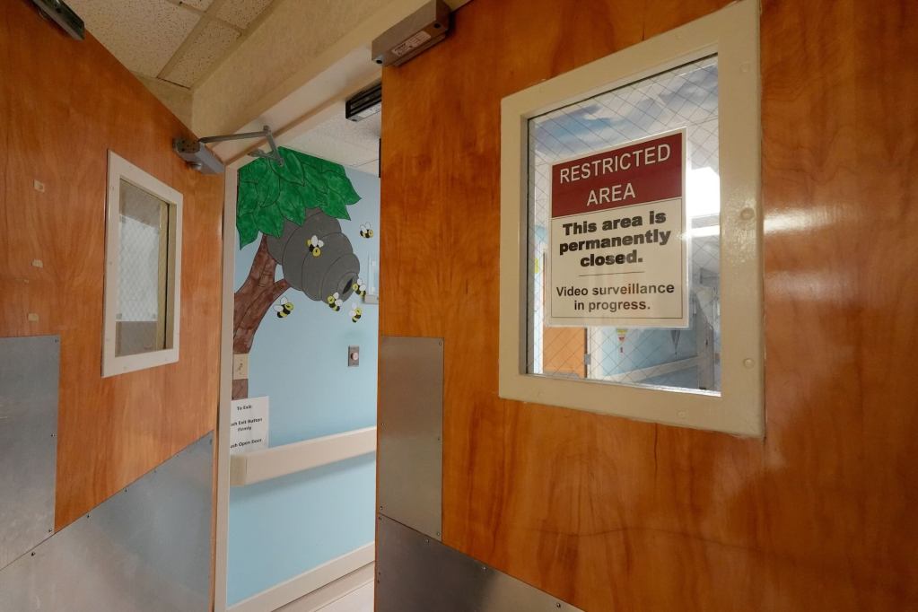 A partially open set of hospital doors labeled 'Restricted Area, This area is permanently closed.' Artwork painted on the wall can be seen beyond