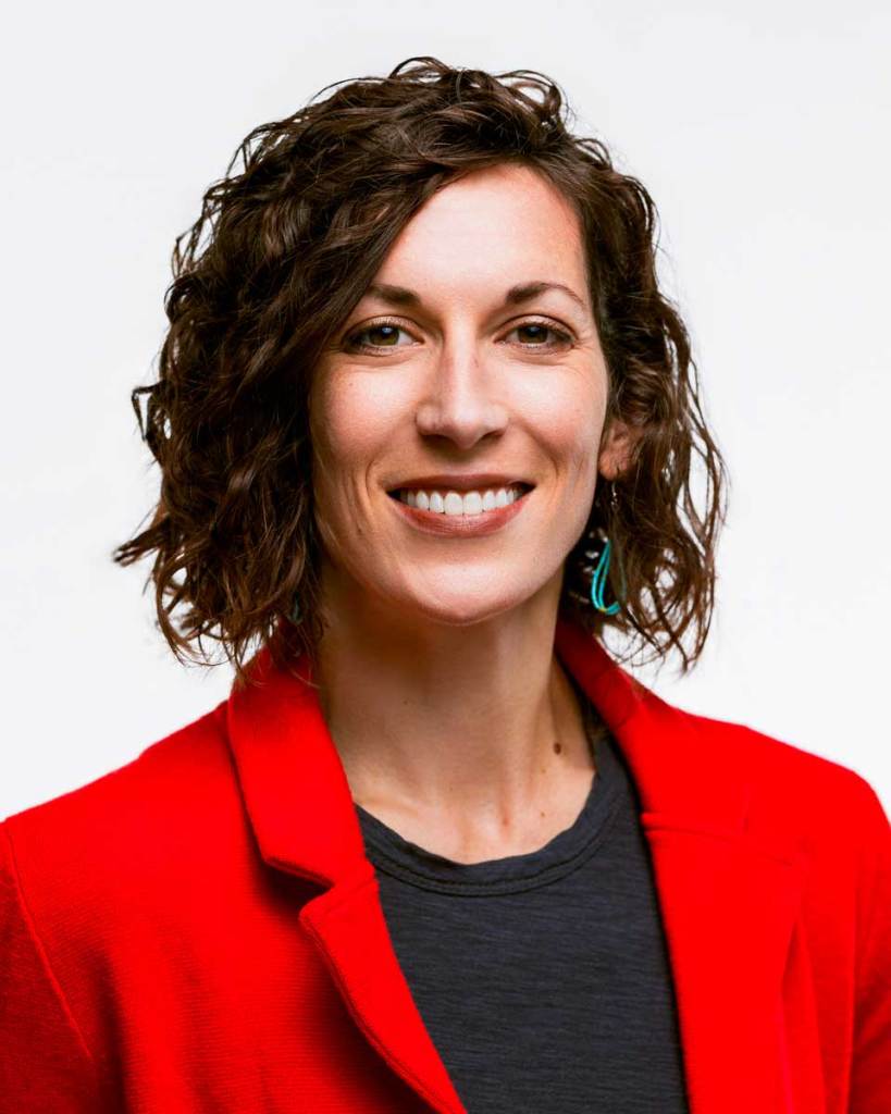 A portrait of a smiling woman with short brown hair, wearing a red blazer over a black top
