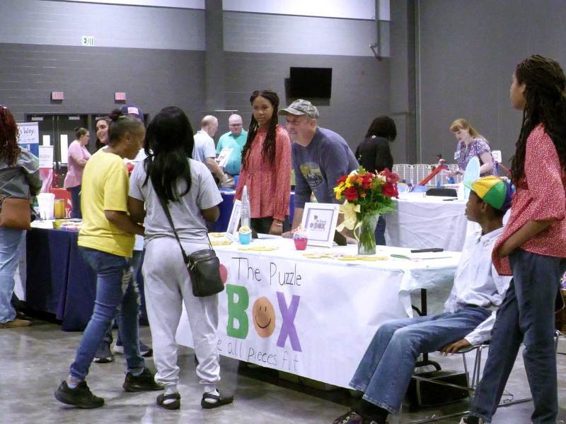 Families and service providers stand near resource tables at an indoor autism resource fair.
