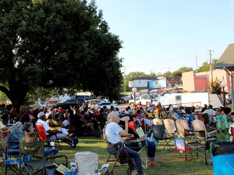 A field filled with people sitting in folding chairs they brought from home, watching an event