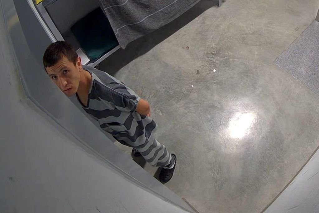 A man in a holding cell looking up toward the camera.