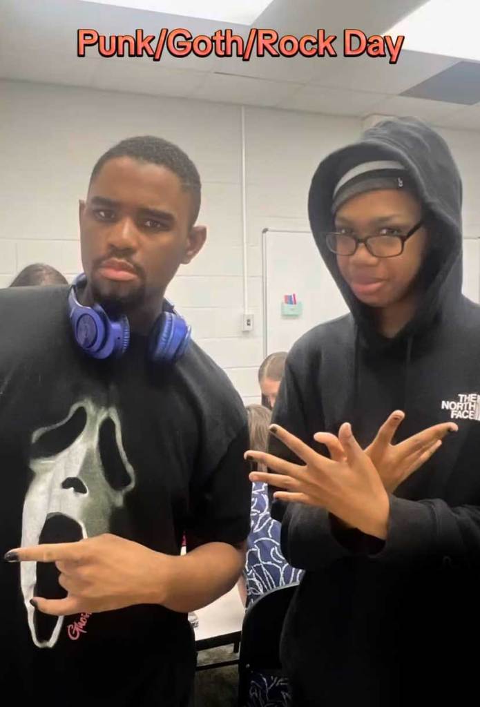Two teens dressed in black pose together for a photo in school. The image is labeled "Punk/Goth/Rock Day"