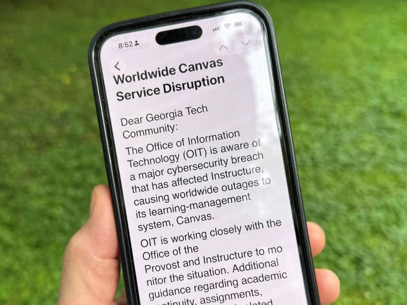A hand holds a mobile phone outside that read 'Worldwide Canvas Service Disruption Dear Georgia Tech Community: The Office of Information Technology (OIT) is aware of a major cybersecurity breach that has affected Instructure, causing worldwide outages to its learning-management system, Canvas. OIT is working closely with the Office of the Provost and Instructure to monitor the situation. Additional guidance regarding academic...'