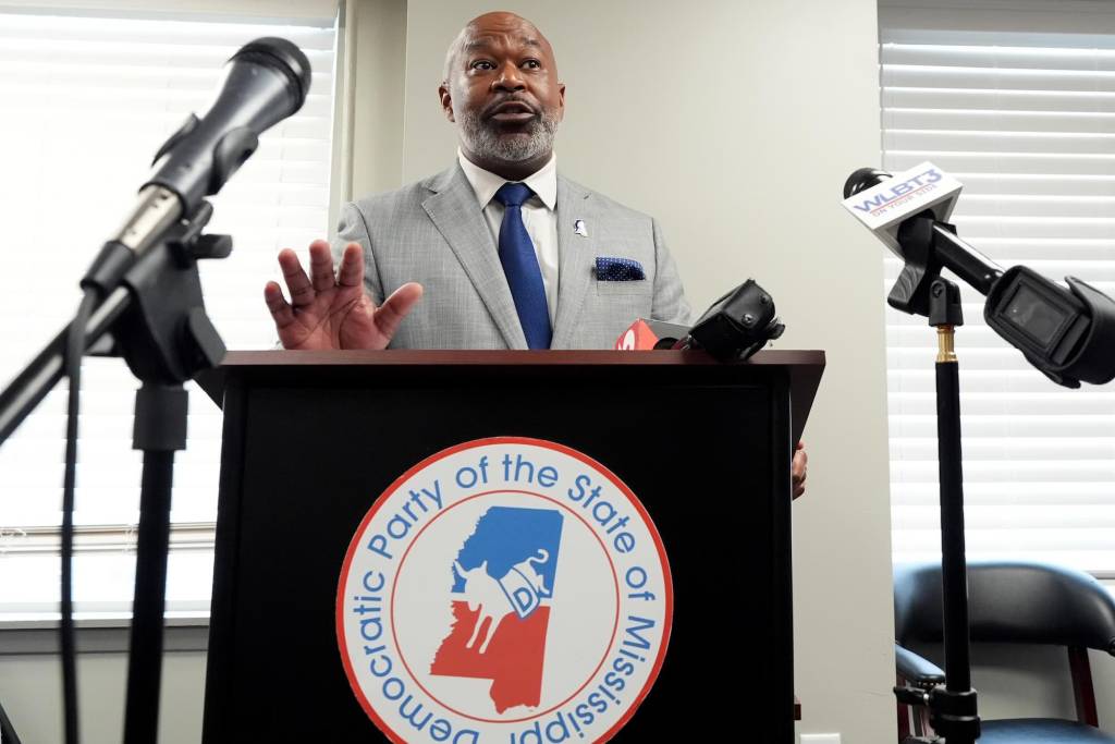 Cheikh Taylor speaking at an event, a sign for the Democratic Party of the State of Mississippi