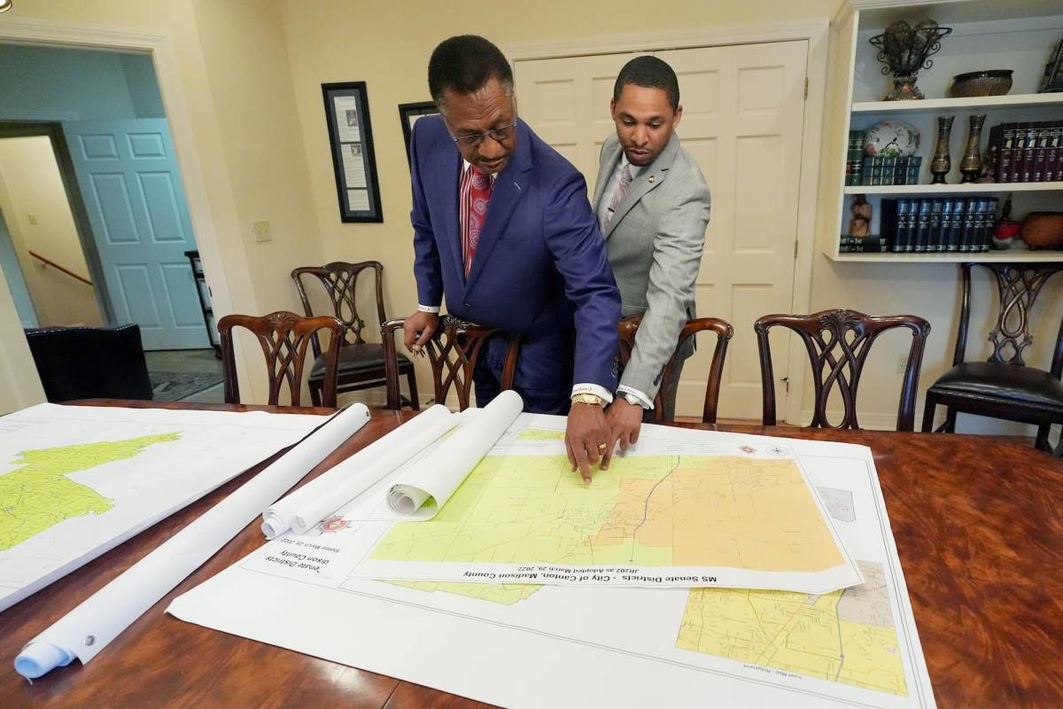 Edward and Bradford Blackmon stand at a table in an office, pointing at something on the first of several stacked maps