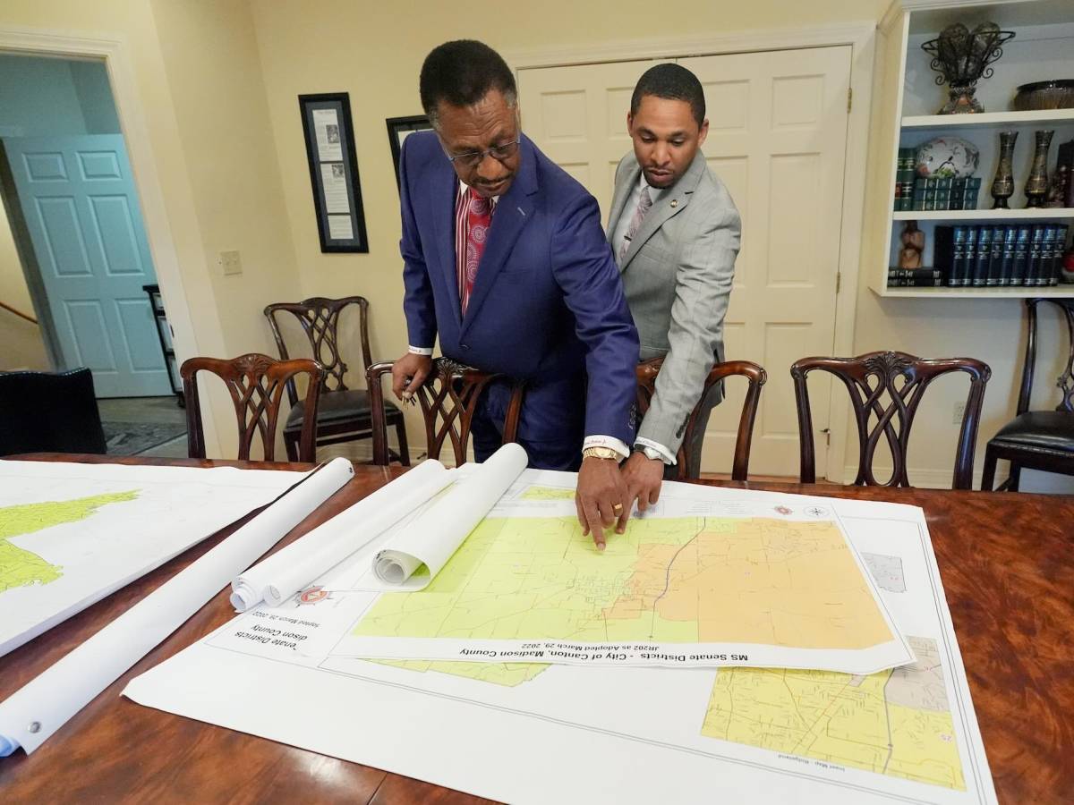 Edward and Bradford Blackmon stand at a table in an office, pointing at something on the first of several stacked maps