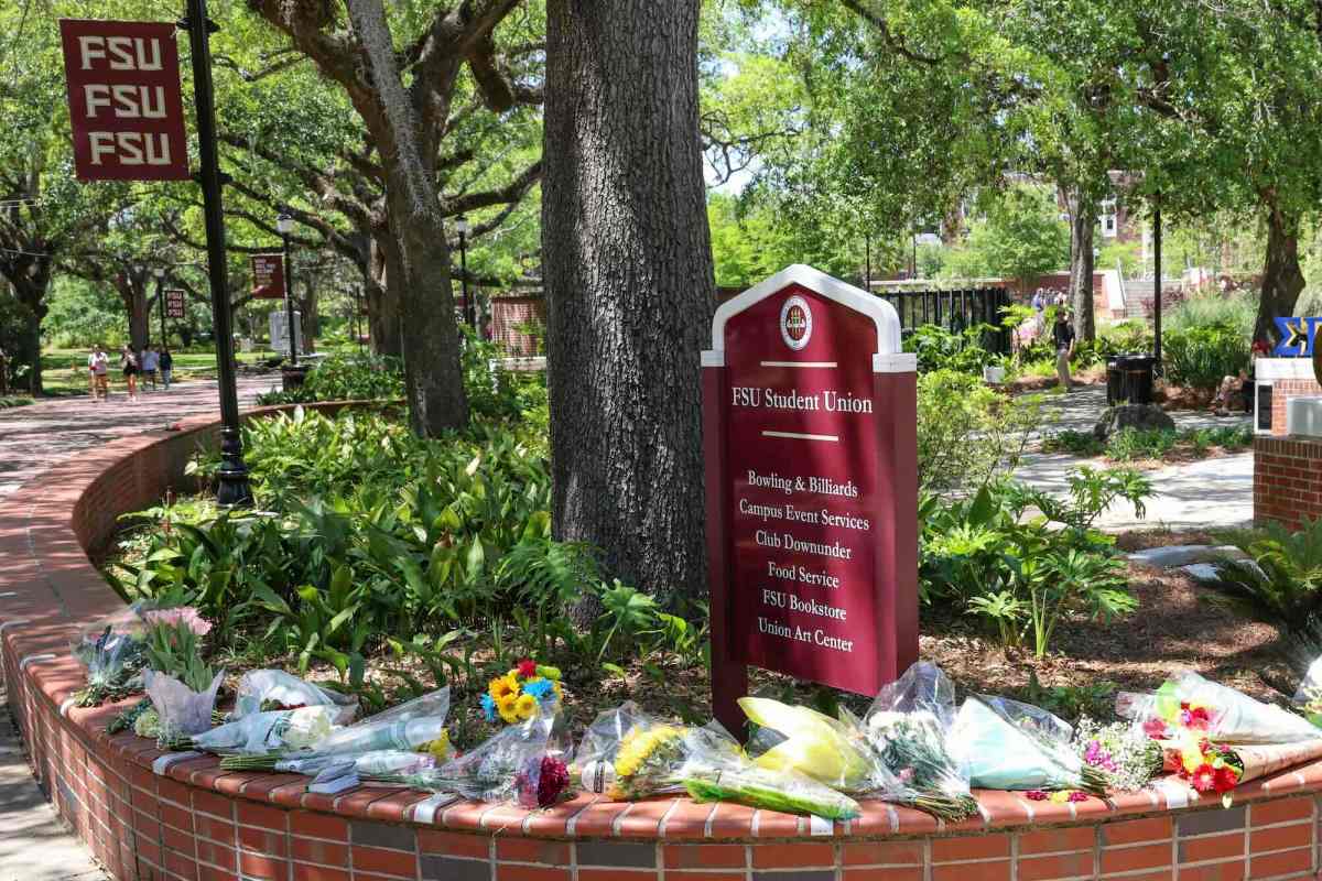 An arrangement of flowers and bouquets in a makeshift memorial in front of a sign at Florida State University that says “FSU Student Union.”