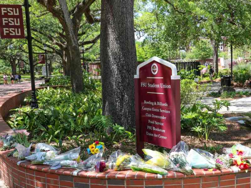 An arrangement of flowers and bouquets in a makeshift memorial in front of a sign at Florida State University that says “FSU Student Union.”