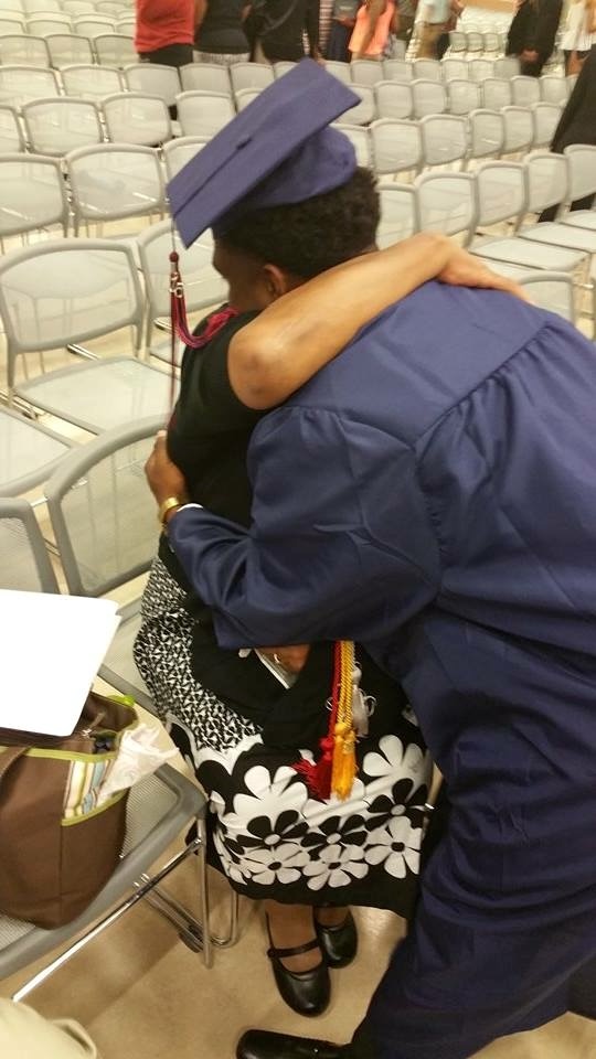 A seated woman hugging a student wearing a blue cap and gown