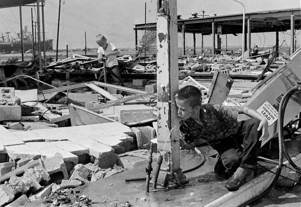 An old black and white photo from the 1960's showing two young boys in the debris of a hurricane wrecked gas station
