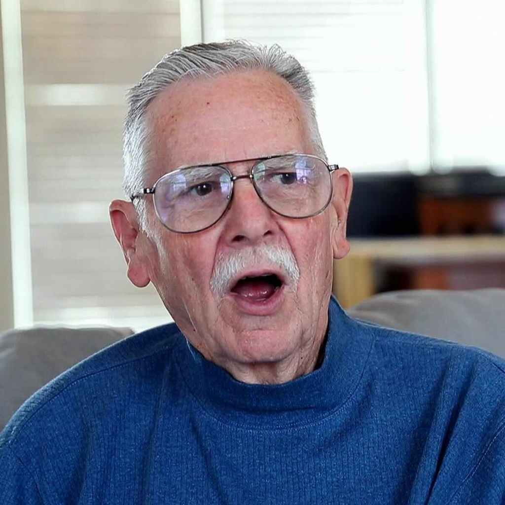 Jack Thornell, wearing blue and seated on a grey couch in a living room, speaking