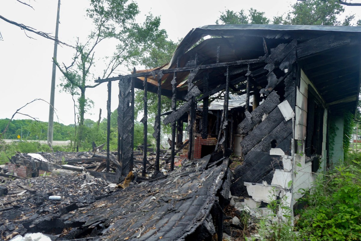 A burnt home at 2816 Kingswood Drive, surrounded by a yard full of tall, overgrown plants.