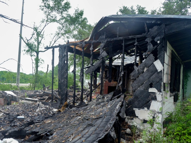 A burnt home at 2816 Kingswood Drive, surrounded by a yard full of tall, overgrown plants.