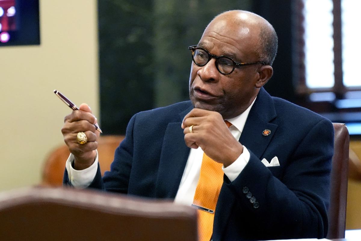 Johnny Dupree, seated in a meeting and talking with both hands before him, one waving a pen as he speaks