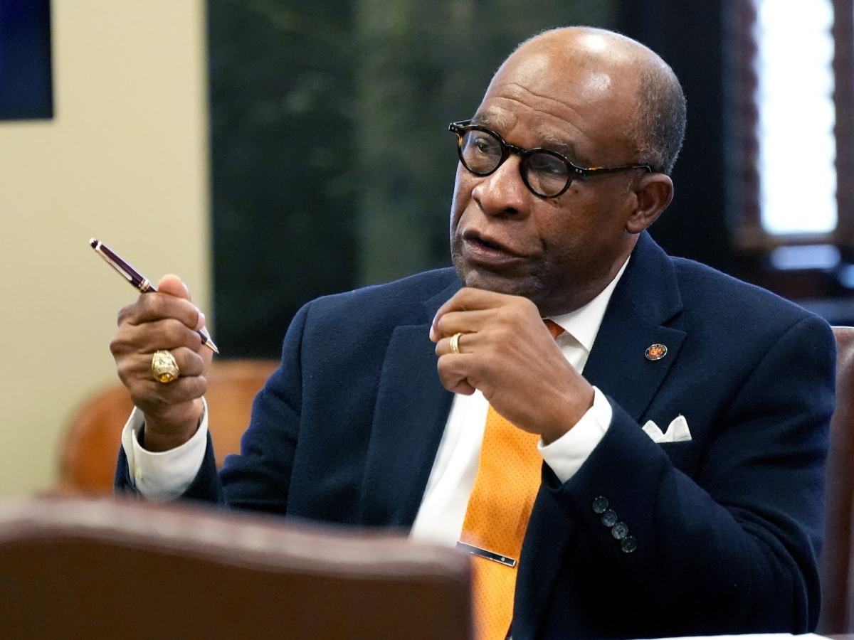 Johnny Dupree, seated in a meeting and talking with both hands before him, one waving a pen as he speaks